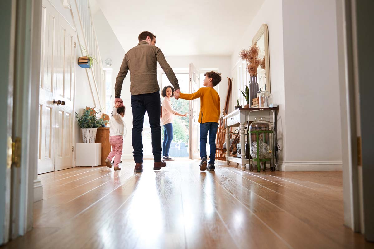 A man holds his childrens' while walking towards their open front door.