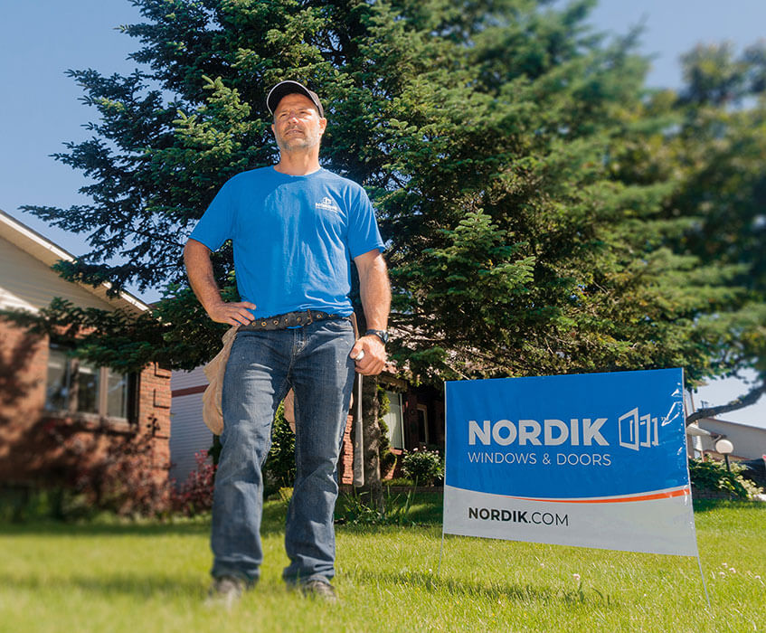 A Nordik window installer poses on the lawn of a house with newly replaced windows.